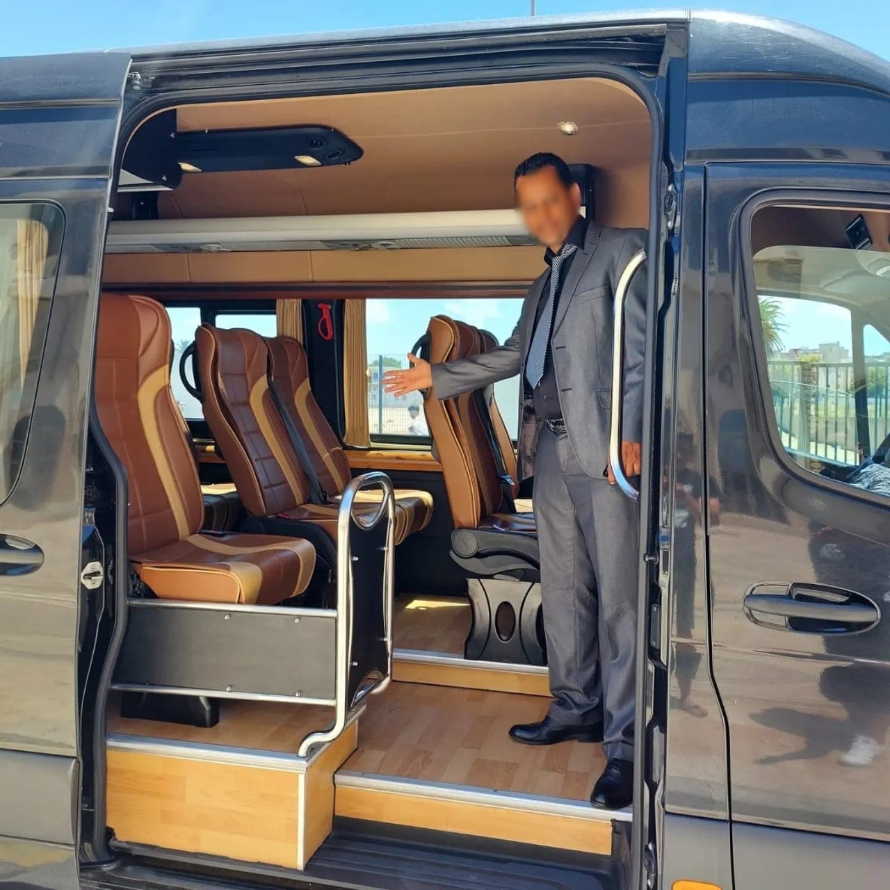 Man in a suit gesturing toward the brown leather interior of a luxury van.