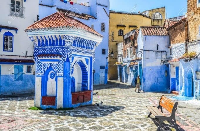 Ornate blue and white fountain in a sunny square surrounded by Chefchaouen's iconic blue buildings.