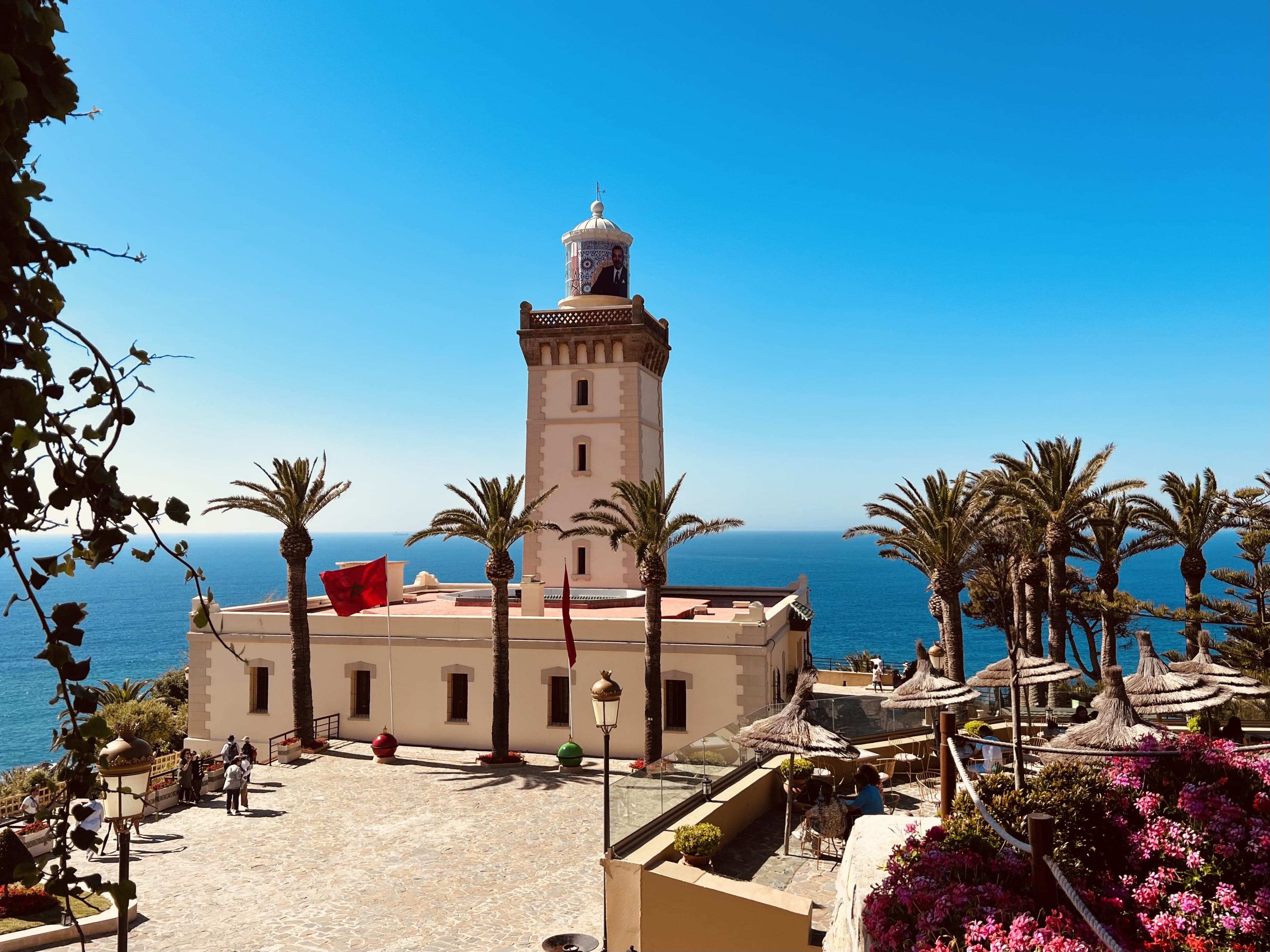Cape Spartel lighthouse in Morocco overlooking the blue ocean with palm trees and red flag.