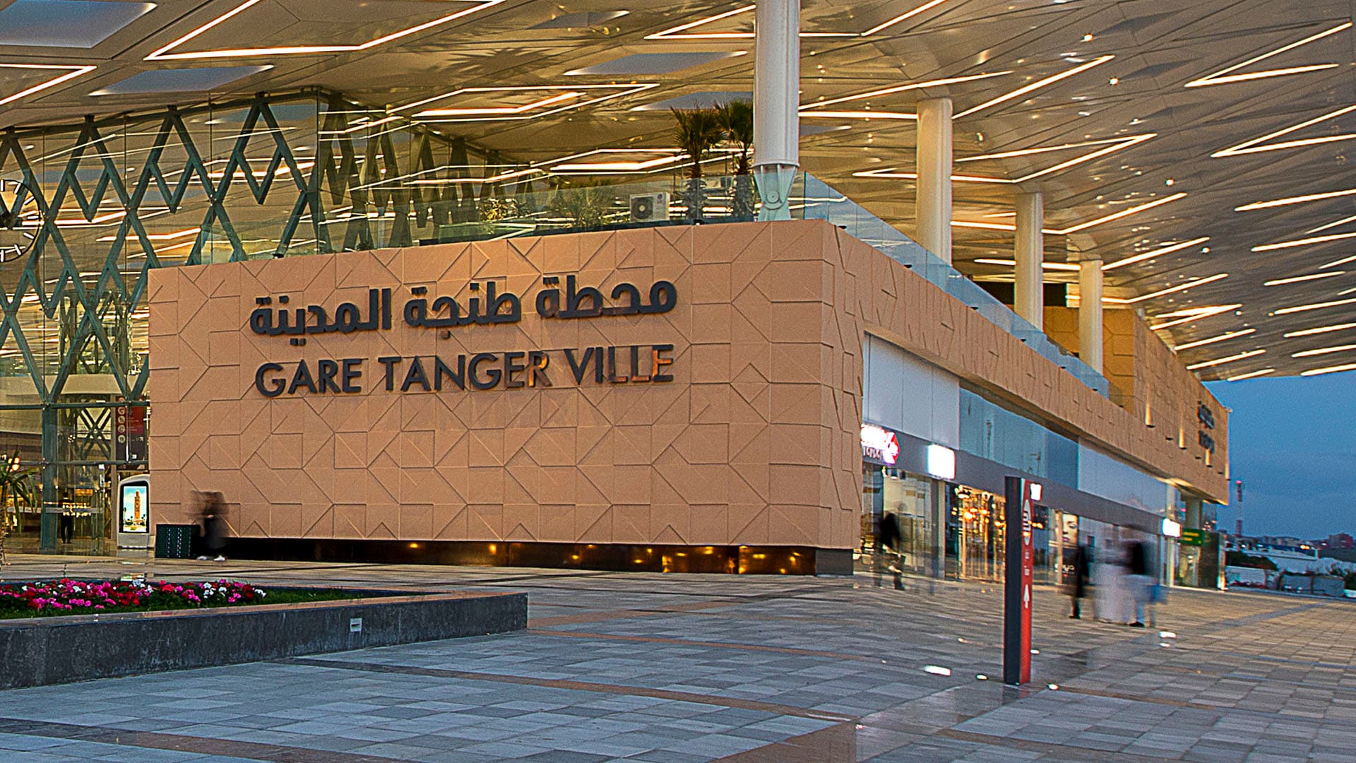 Modern Gare Tanger Ville train station with an illuminated geometric canopy and textured facade at dusk.