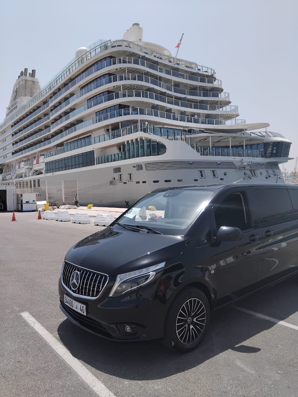 Black Mercedes van parked in front of a massive white cruise ship at port.