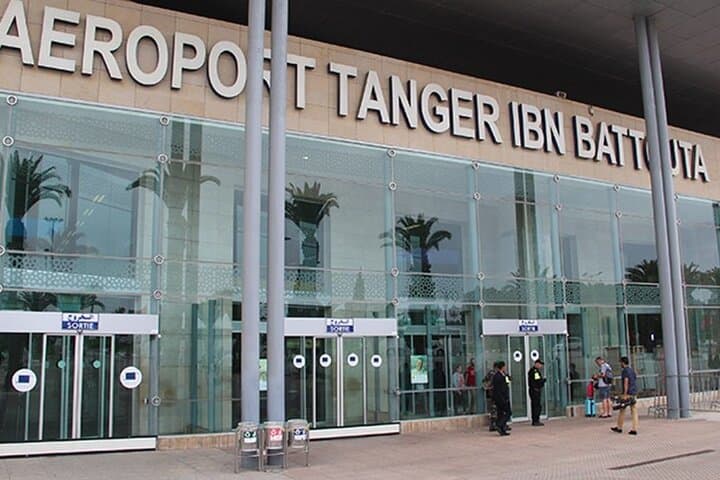 Modern glass facade of Tanger Ibn Battouta Airport with people standing near the exit.