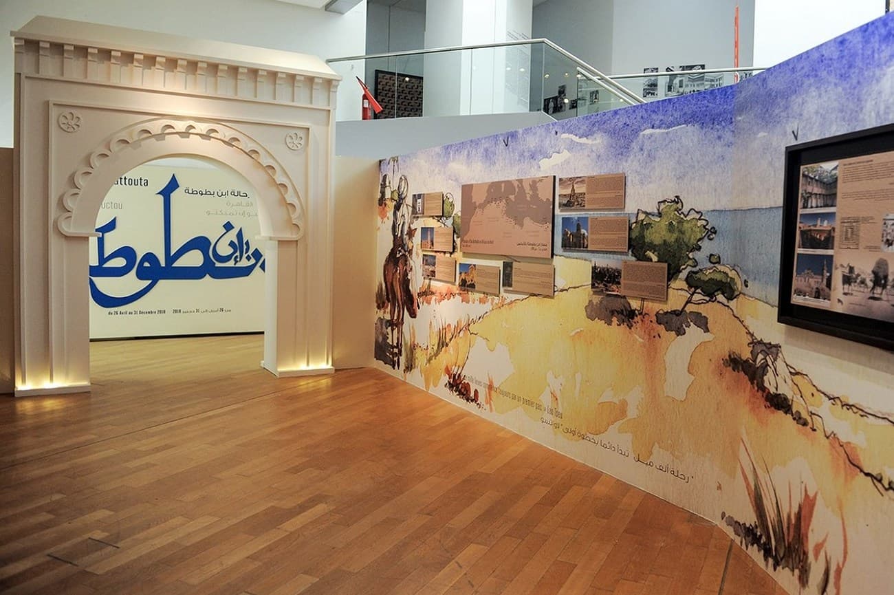 Exhibition space featuring a white arched doorway and a mural wall illustrating Ibn Battuta's travels.