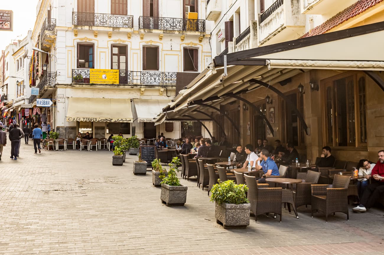 People relaxing at an outdoor cafe on a cobblestone street with historic Mediterranean architecture.